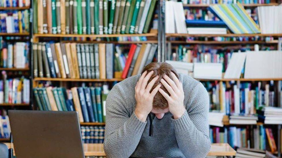 Man studying in library holding head in his hands