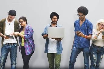 Group of young adults looking at cell phones and laptops