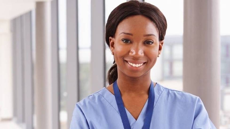 Nurse in blue scrubs smiling and standing in hospital hallway